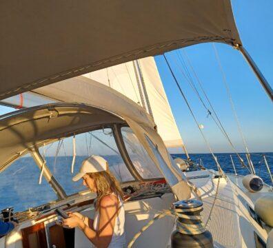Woman seated in the cockpit a sailing yacht during a Greek island cruise at sunset.
