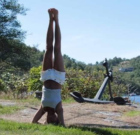 A person practicing a headstand on a grassy area outdoors near a large anchor.